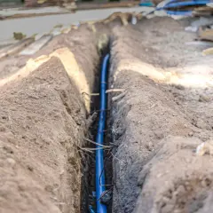Wykop pod instalację, gdzie widać niebieską rurę. W tle materiały budowlane i ziemia. Prawdopodobnie to poniemieckie kable w ziemi.