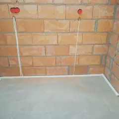 Przewody w posadzce bez peszla, przygotowane do dalszych prac instalacyjnych. Widoczne puszki elektryczne w ścianie z cegły.