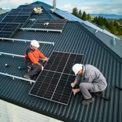 Dwóch mężczyzn montuje instalację fotowoltaiczną na dachu. Panele słoneczne zapewnią czystą energię.