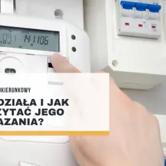Palec wskazuje na ekran licznika dwukierunkowego, pokazując jego odczyty. Obok widoczne są bezpieczniki.