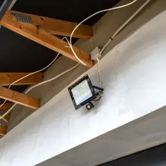 Nowoczesna elektryka w garażu: jasny reflektor LED z czujnikiem ruchu zamontowany na betonowej belce, otoczony drewnianą konstrukcją dachu i białymi przewodami.