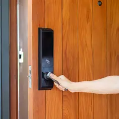 Dłoń otwiera drzwi z nowoczesnym elektrozaczepem z czujnikiem otwarcia.