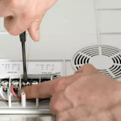 Ręce majsterkowicza podłączają przewód do płyty indukcyjnej, dokręcając śruby śrubokrętem.