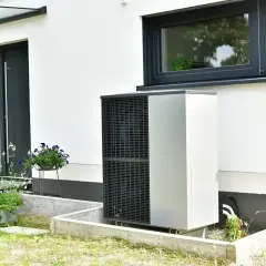 Pompa ciepła zainstalowana przy nowoczesnym domu z białym tynkiem i dużym oknem.