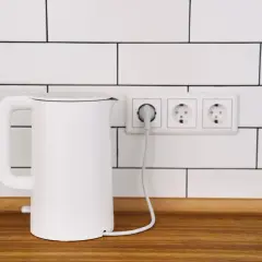 Biały czajnik elektryczny podłączony do gniazdka. Zastanawiasz się, co pobiera więcej prądu: czajnik elektryczny czy płyta indukcyjna?