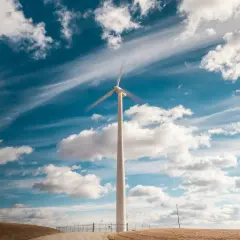 Wiatrak na tle błękitnego nieba z chmurami. Symbol inwestycji w OZE i czystej energii.