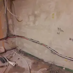 Skrętka obok kabla elektrycznego biegnie wzdłuż ściany. Na tynku widoczne oznaczenia "77cm" i "32J".