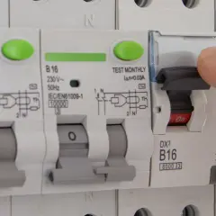 Dłoń naciska dźwignię wyłącznika, który jest częścią instalacji elektrycznej. Czy różnicówka jest obowiązkowa? To pytanie o bezpieczeństwo.