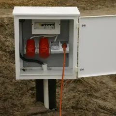 Biała skrzynka z bezpiecznikami i gniazdami, stanowiąca przyłącze elektryczne do domu. Pomarańczowy kabel wychodzi z gniazdka.