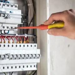 Elektryk naprawia instalację, gdzie różnicówka wybija pod obciążeniem. Widać bezpieczniki i przewody.