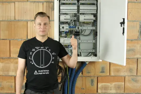 Elektryk pokazuje rozdzielnicę, odpowiadając na pytanie, ile różnicówek w domu jest bezpieczne.