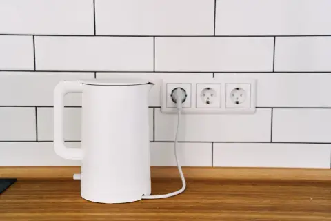 Biały czajnik elektryczny podłączony do gniazdka. Zastanawiasz się, co pobiera więcej prądu: czajnik elektryczny czy płyta indukcyjna?