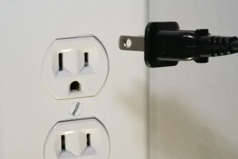 Zalane gniazdko elektryczne. Czarny wtyk zbliża się do białej obudowy, grożąc zwarciem.