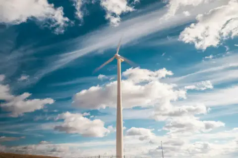 Wiatrak na tle błękitnego nieba z chmurami. Symbol inwestycji w OZE i czystej energii.