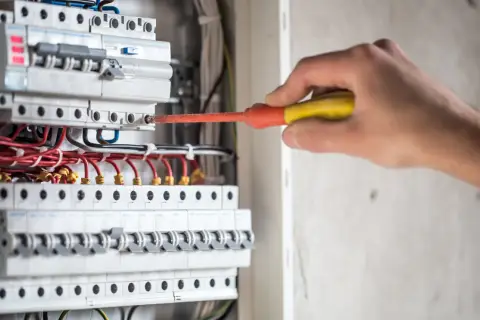 Elektryk naprawia instalację, gdzie różnicówka wybija pod obciążeniem. Widać bezpieczniki i przewody.
