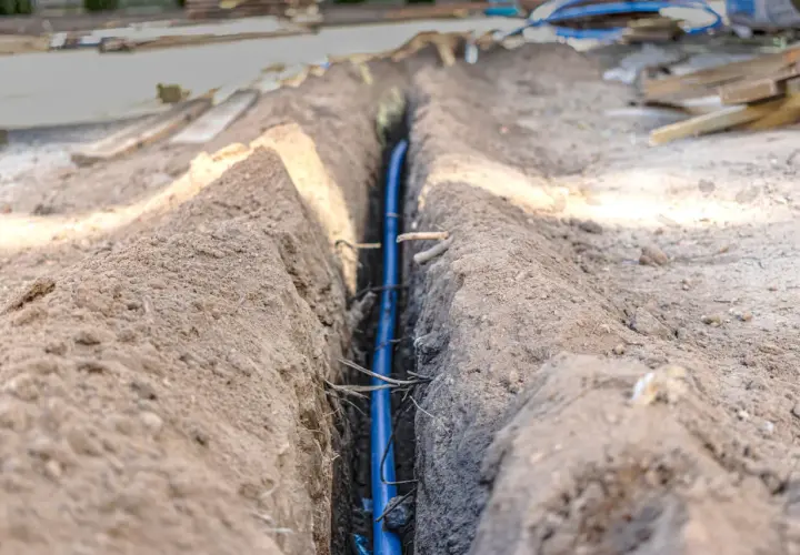 Wykop pod instalację, gdzie widać niebieską rurę. W tle materiały budowlane i ziemia. Prawdopodobnie to poniemieckie kable w ziemi.