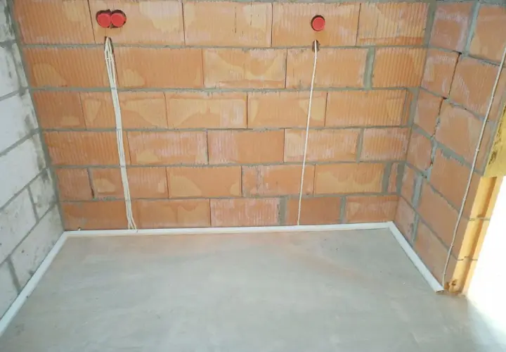 Przewody w posadzce bez peszla, przygotowane do dalszych prac instalacyjnych. Widoczne puszki elektryczne w ścianie z cegły.
