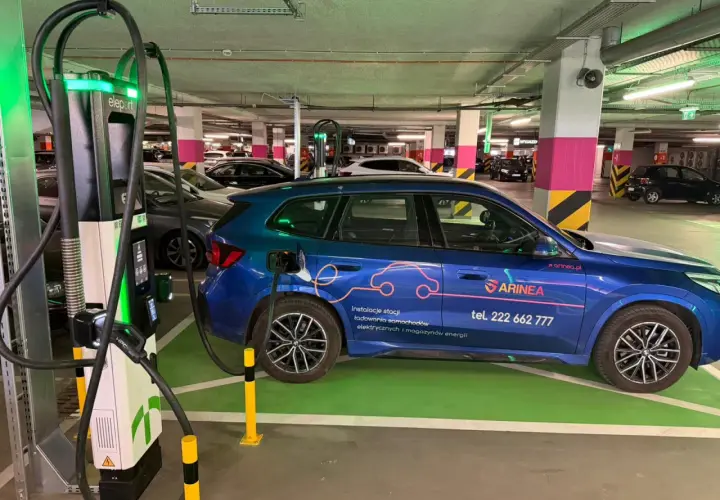 Niebieski samochód elektryczny ładuje się przy stacji typu wallbox w podziemnym parkingu. To przyszłość transportu!