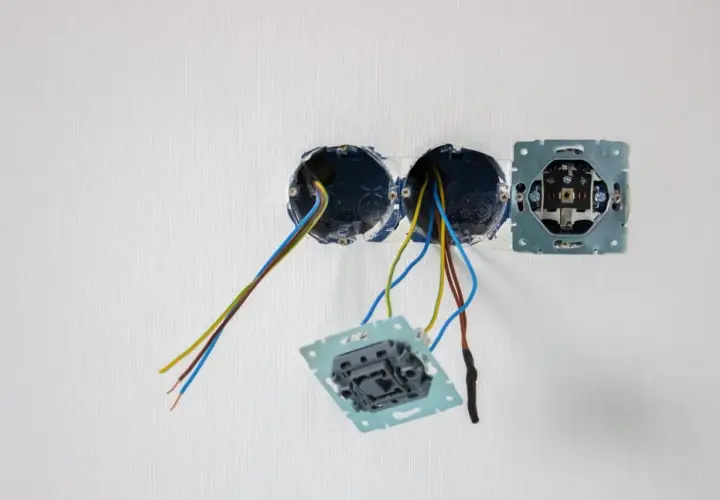 Osadzanie puszek elektrycznych w białej ścianie. Widać przewody wychodzące z dwóch puszek, a obok zamontowaną ramkę gniazdka.