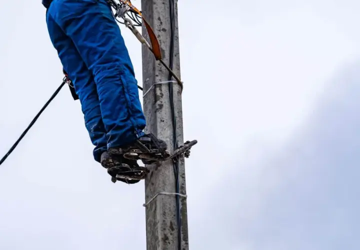 Energetyka chce zakopać kabel na mojej działce. Pracownik na słupie w niebieskich spodniach i z przyrządami.