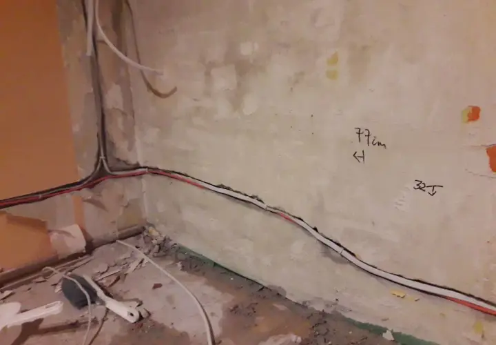 Skrętka obok kabla elektrycznego biegnie wzdłuż ściany. Na tynku widoczne oznaczenia "77cm" i "32J".