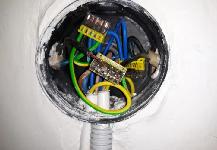 Widoczne przewody elektryczne w puszce, połączone złączkami. Brak zera w gniazdku może być przyczyną problemów z instalacją.