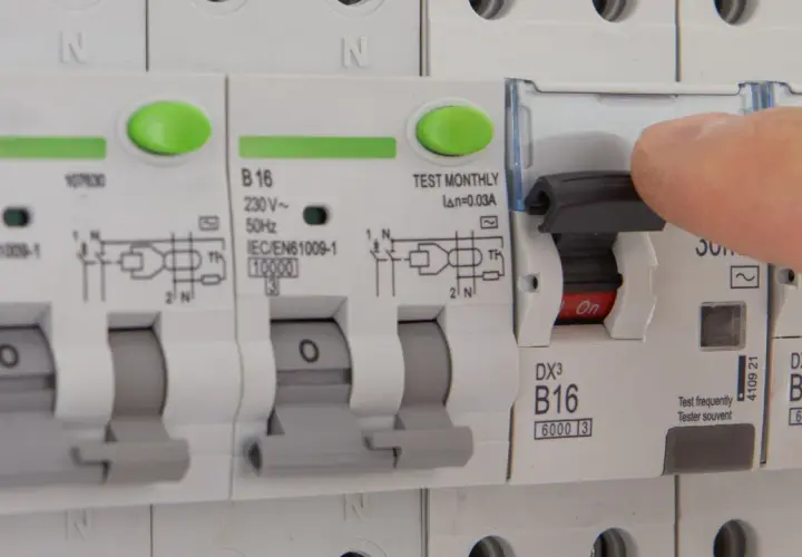 Dłoń naciska dźwignię wyłącznika, który jest częścią instalacji elektrycznej. Czy różnicówka jest obowiązkowa? To pytanie o bezpieczeństwo.
