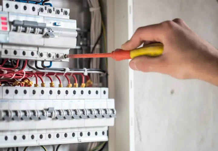 Elektryk naprawia instalację, gdzie różnicówka wybija pod obciążeniem. Widać bezpieczniki i przewody.