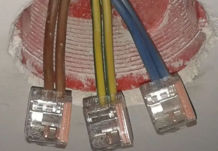Żółto-zielony kabel oznacza uziemienie, kluczowy dla bezpieczeństwa instalacji elektrycznej. Widać go obok brązowych i niebieskich przewodów w puszkach.
