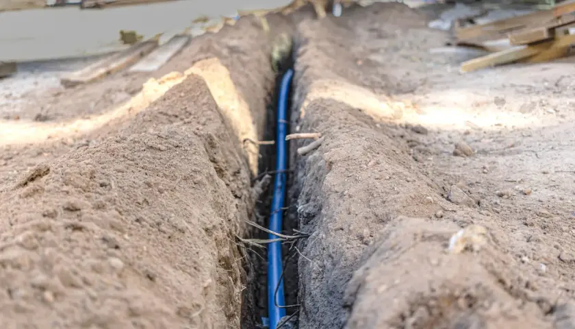 Wykop pod instalację, gdzie widać niebieską rurę. W tle materiały budowlane i ziemia. Prawdopodobnie to poniemieckie kable w ziemi.