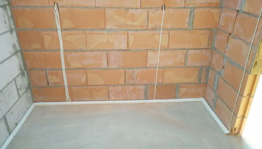 Przewody w posadzce bez peszla, przygotowane do dalszych prac instalacyjnych. Widoczne puszki elektryczne w ścianie z cegły.
