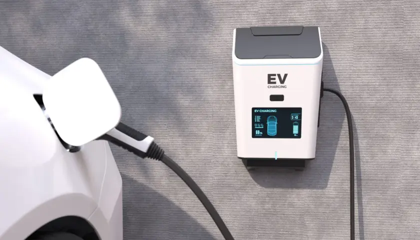 Ładowanie samochodu elektrycznego w domu. Stacja EV na ścianie, kabel podłączony do białego auta, bateria naładowana w 69%.