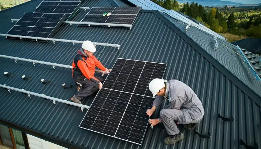 Dwóch mężczyzn montuje instalację fotowoltaiczną na dachu. Panele słoneczne zapewnią czystą energię.