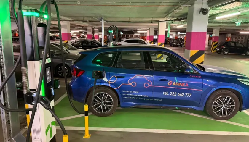 Niebieski samochód elektryczny ładuje się przy stacji typu wallbox w podziemnym parkingu. To przyszłość transportu!