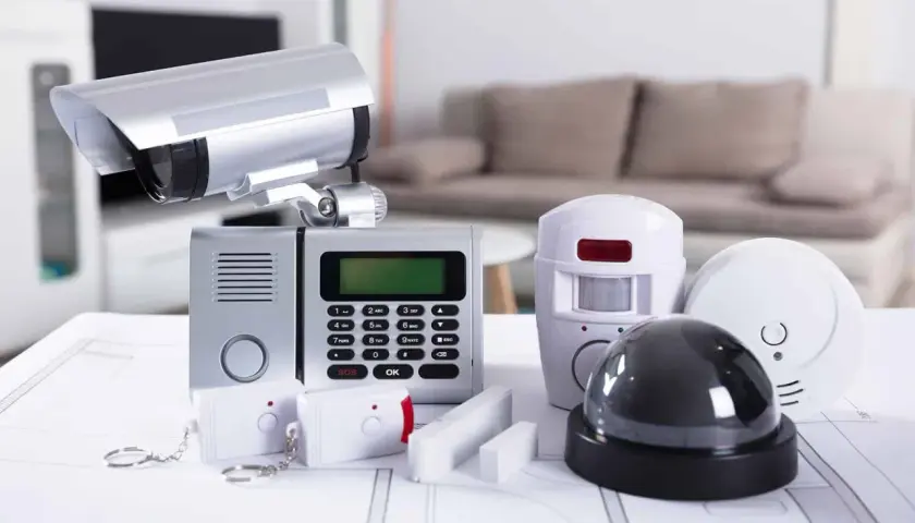 System alarmowy do monitoringu zewnętrznego domu jednorodzinnego przewodowego: kamera, panel sterowania, czujniki ruchu, dymu i klucze.