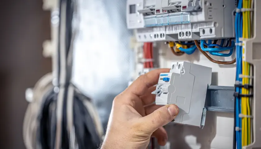Dłoń montuje bezpiecznik w skrzynce elektrycznej. Widać przewody i inne zabezpieczenia. Czy to bezpiecznik b czy c?