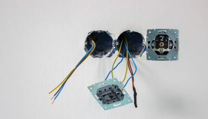 Osadzanie puszek elektrycznych w białej ścianie. Widać przewody wychodzące z dwóch puszek, a obok zamontowaną ramkę gniazdka.