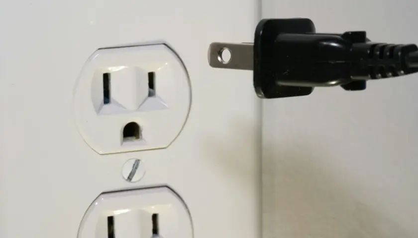Zalane gniazdko elektryczne. Czarny wtyk zbliża się do białej obudowy, grożąc zwarciem.