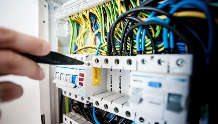 Ręka z narzędziem przy skrzynce z bezpiecznikami i przewodami. Kluczowe dla planowania elektryki w domu.