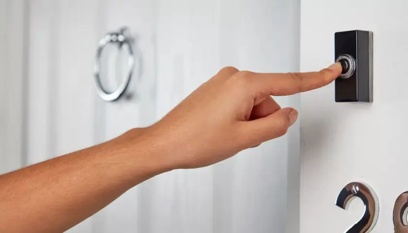 Dłoń naciska fajny dzwonek do drzwi. Obok widoczny numer 28.