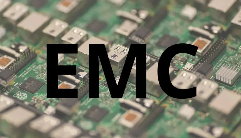 Na zielonej płytce drukowanej z widocznymi elementami elektronicznymi, wielkimi czarnymi literami widnieje napis "EMC". To skrót od Electromagnetic Compatibility, czyli kompatybilności elektromagnetycznej.