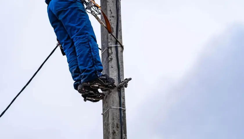 Energetyka chce zakopać kabel na mojej działce. Pracownik na słupie w niebieskich spodniach i z przyrządami.