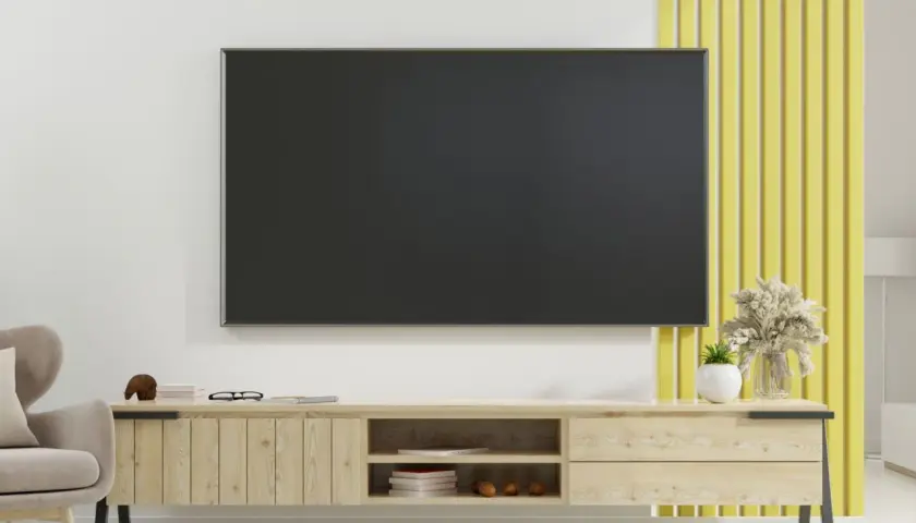 Nowoczesny salon z telewizorem na ścianie, pod którym znajduje się drewniana szafka. Prowadzenie kabli po ścianie jest dyskretne.