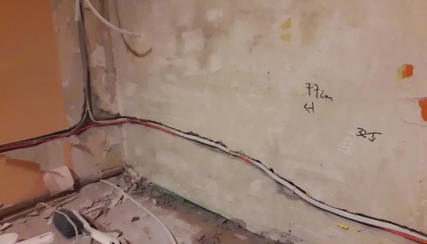 Skrętka obok kabla elektrycznego biegnie wzdłuż ściany. Na tynku widoczne oznaczenia "77cm" i "32J".