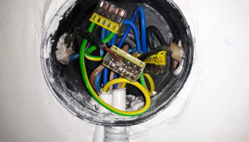 Widoczne przewody elektryczne w puszce, połączone złączkami. Brak zera w gniazdku może być przyczyną problemów z instalacją.