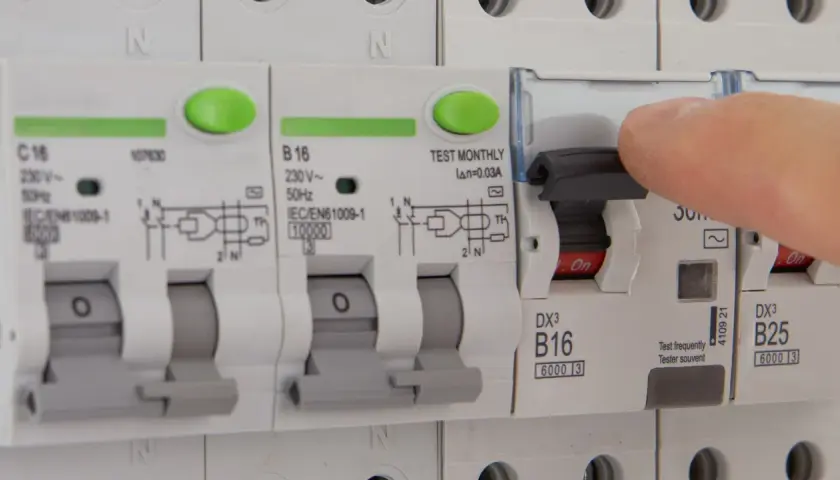 Dłoń naciska dźwignię wyłącznika, który jest częścią instalacji elektrycznej. Czy różnicówka jest obowiązkowa? To pytanie o bezpieczeństwo.
