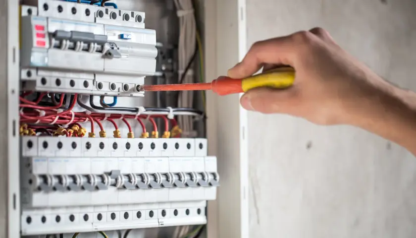 Elektryk naprawia instalację, gdzie różnicówka wybija pod obciążeniem. Widać bezpieczniki i przewody.