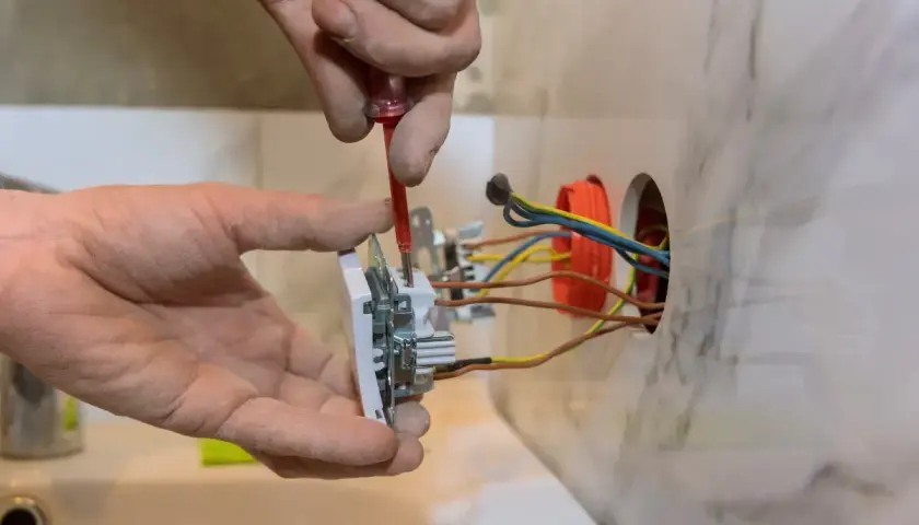 Elektryk montuje gniazdko, podłączając przewody zgodnie ze schematem. Widać fragment instalacji elektrycznej.