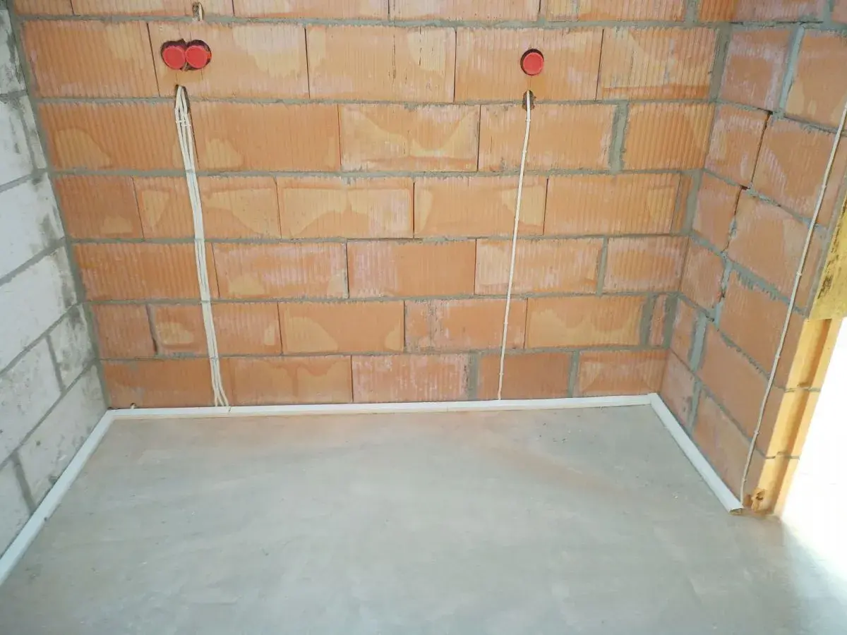 Przewody w posadzce bez peszla, przygotowane do dalszych prac instalacyjnych. Widoczne puszki elektryczne w ścianie z cegły.