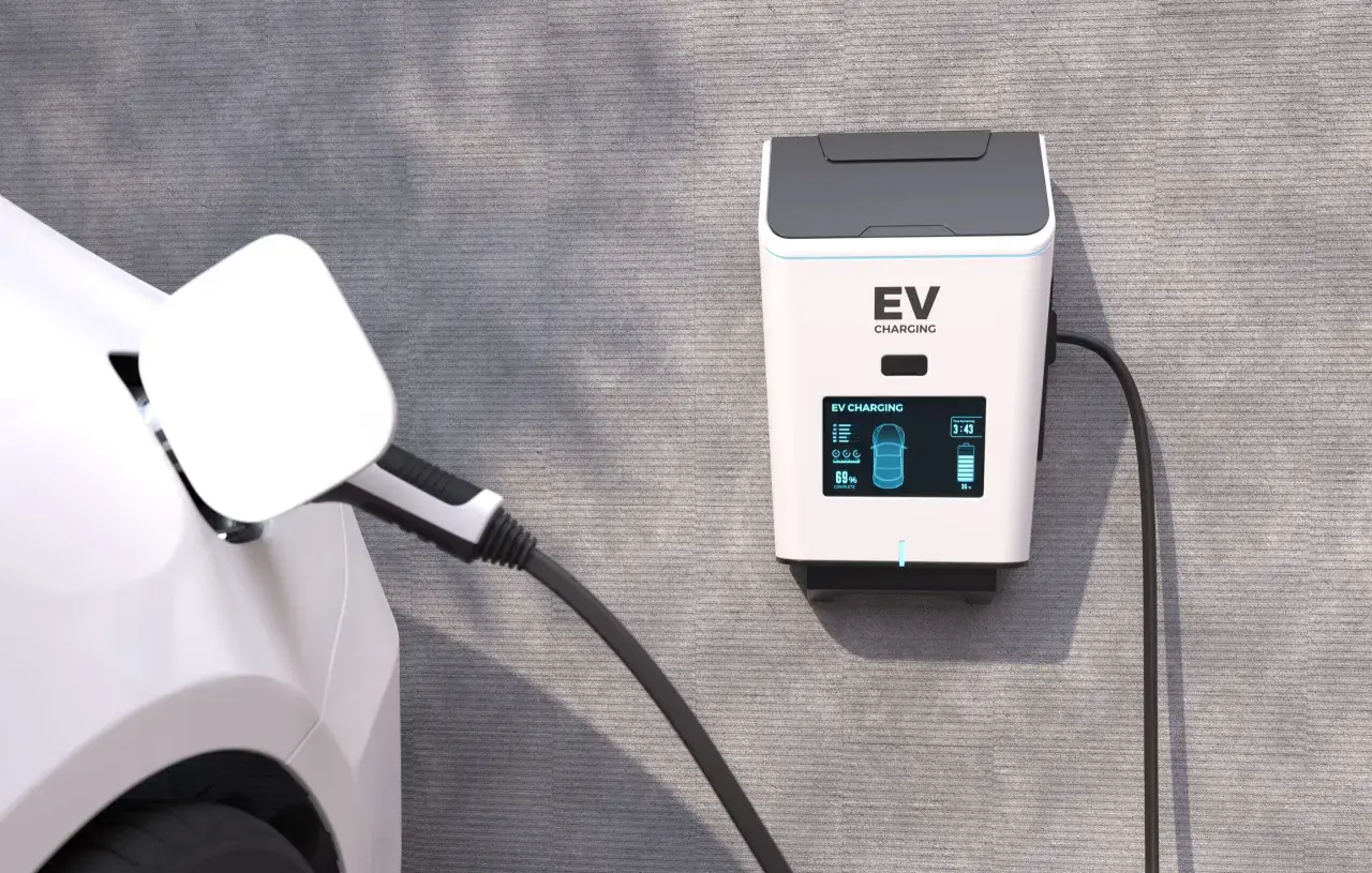 Ładowanie samochodu elektrycznego w domu. Stacja EV na ścianie, kabel podłączony do białego auta, bateria naładowana w 69%.